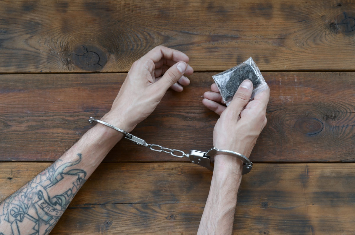 Male Hands Locked In Handcuffs Holding A Plastic Of Marijuana - Cannabis Legalisation - Cannabiz